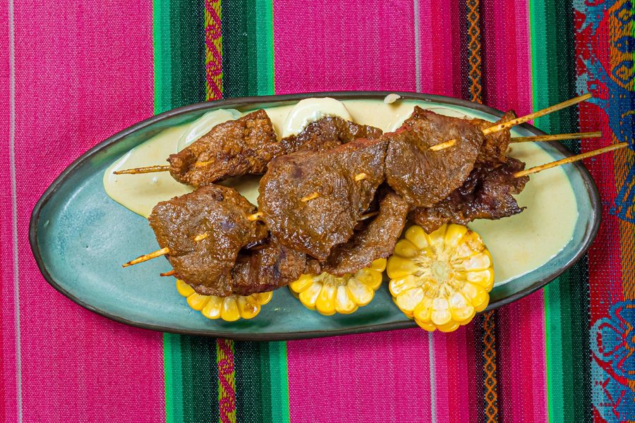 Anticuchos vistos desde arriba, sobre choclo y salsa huancaína